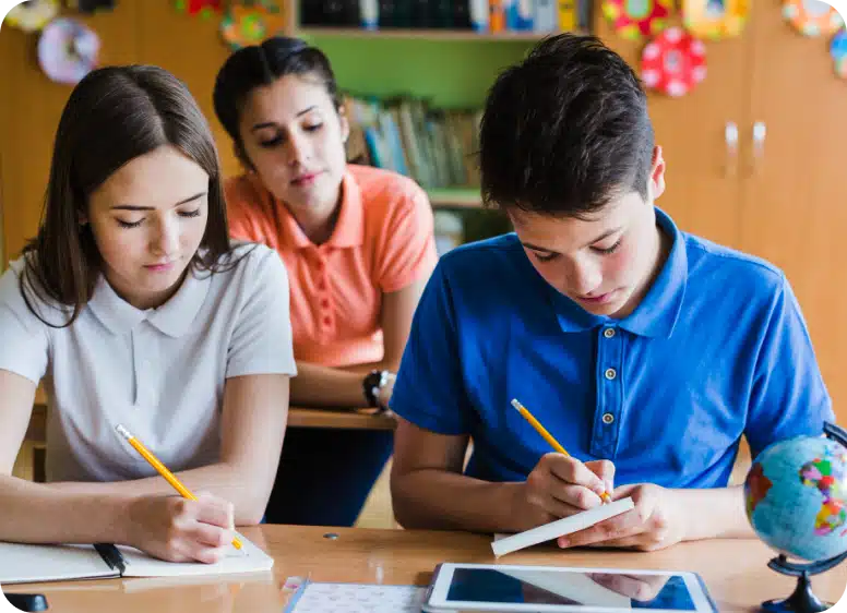 Teacher guiding two students as they write in notebooks