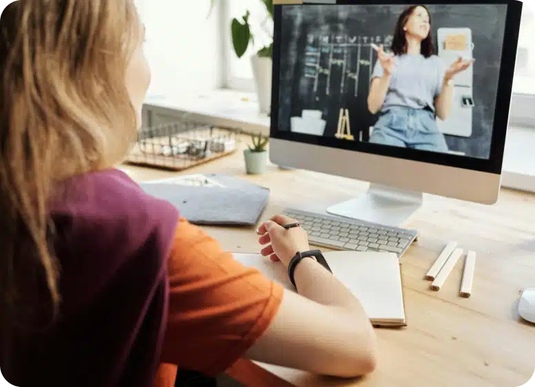 A student attending an online lesson, watching a teacher explain concepts on a computer screen.