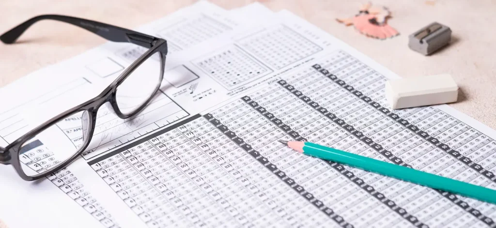 Standardized test answer sheets placed on a desk with eyeglasses, a pencil, and erasers beside them